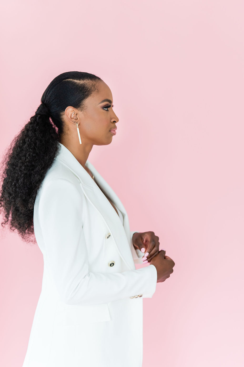Black woman in a white blazer standing confidently against a soft pink background, symbolizing leadership and clarity.