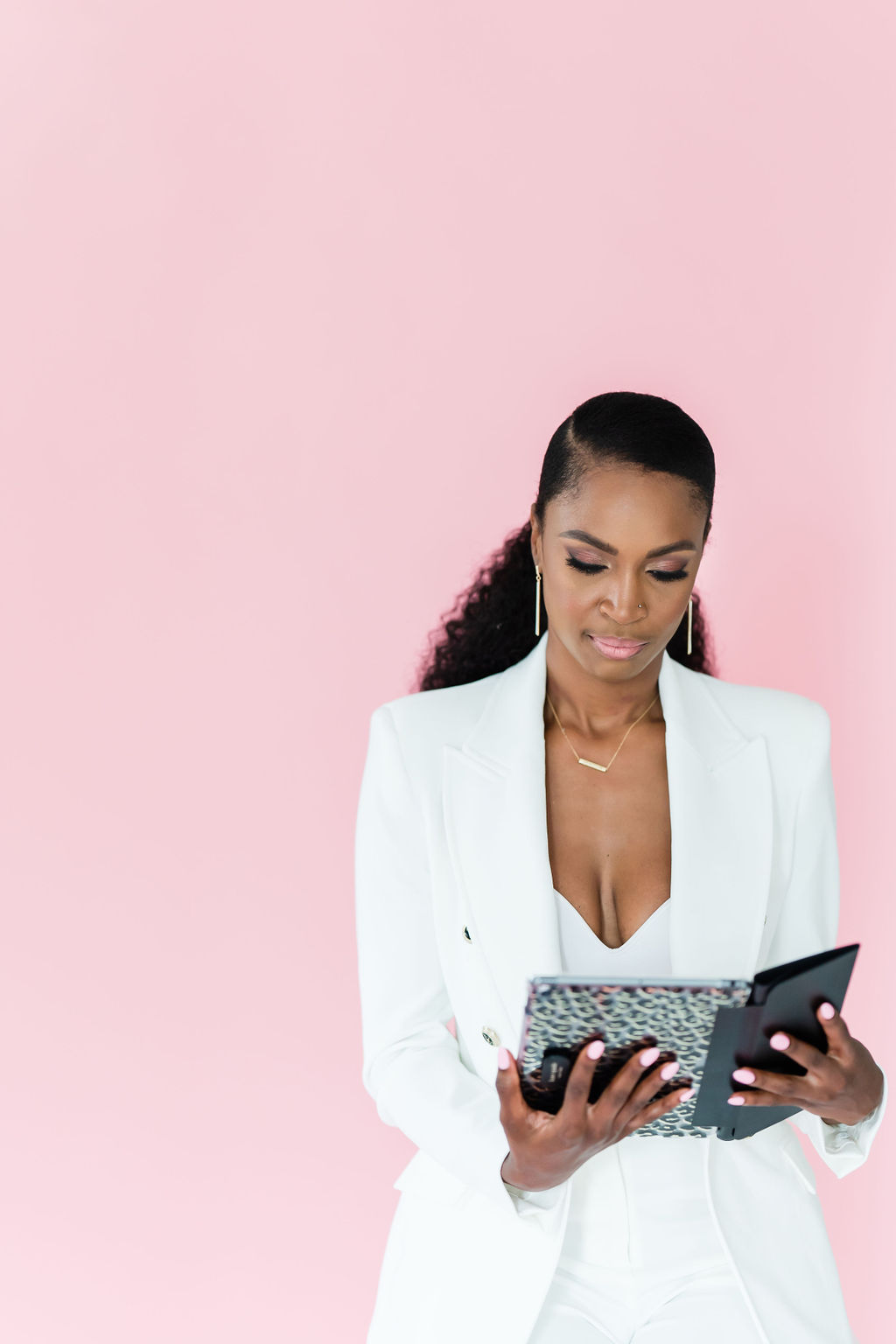 Woman in white suit reflecting while reading a journal, standing against a pink background